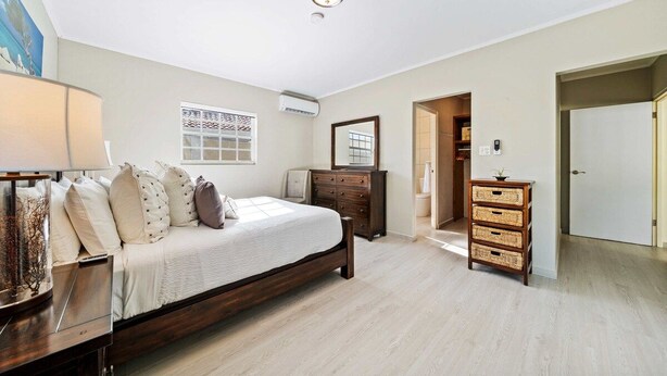 A bedroom with a bed, dresser, and a mirror. There is a window with a view, an air conditioning unit, and a lamp. - Private Pool & Patio Haven, 3BR House near Beach (Noord)
