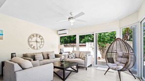 A modern living room with a sofa set, a coffee table, a hanging chair, and a ceiling fan. - Private Pool & Patio Haven, 3BR House near Beach (Noord)