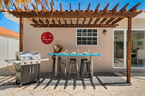An outdoor patio with a grill, a table, and three stools. - Private Pool & Patio Haven, 3BR House near Beach (Noord)