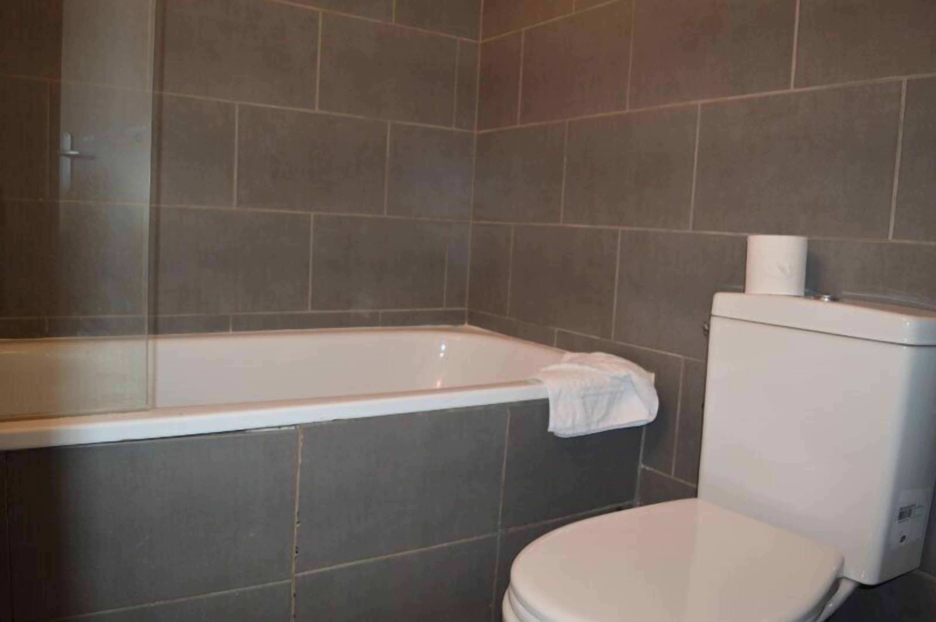Ein Badezimmer mit einer Badewanne, Toilette und gefliesten Wänden.