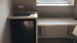 A compact kitchenette with a built-in stove, a small refrigerator, and a window above a countertop. - Appart'Hotel Voltaire  (Chateauroux)