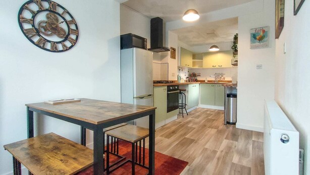 A compact kitchen with a wooden table and bench, a microwave, and a refrigerator. - Bramble Cottage Rhondda Valley by STAE-Homes (Tylorstown)