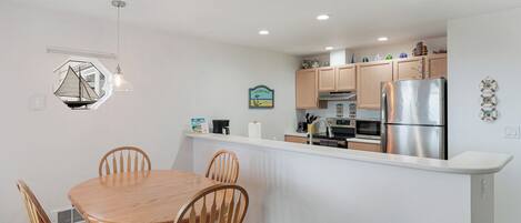 A modern kitchen with a central island, wooden chairs, and a pendant light.