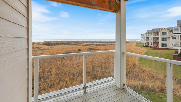 A balcony with a view of a grassy field and a building in the distance. - 423 - To the Ocean and Beyond - Breathtaking Condo (Westport)