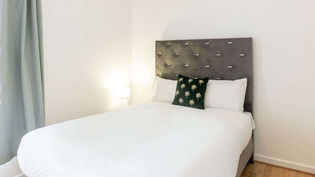 A neatly made bed with white bedding, a grey headboard, and a single decorative pillow with a palm tree pattern. - Host & Stay | Bardsay Road (Liverpool)