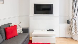 A modern living room with a grey sofa, red cushion, white coffee table, and a flat-screen TV mounted on the wall. - Host & Stay | Bardsay Road (Liverpool)