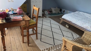 A cozy bedroom with a sloped ceiling, a wooden desk, a bed with a patterned bedspread, and a wicker chair.