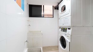 A compact laundry room with a stacked washer and dryer, a small sink, and a window above the dryer.
