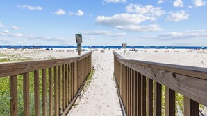 Een houten pad dat naar een strand leidt, met parasols en mensen op het strand.