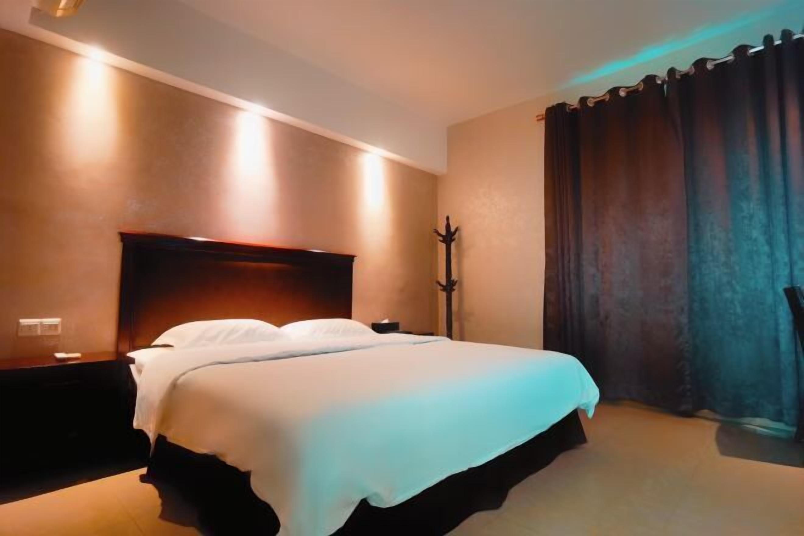 A hotel room with a large bed, a nightstand, a lamp, and a curtain.