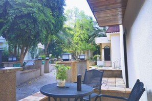 An outdoor patio with a round table and chairs, surrounded by stone walls and potted plants.