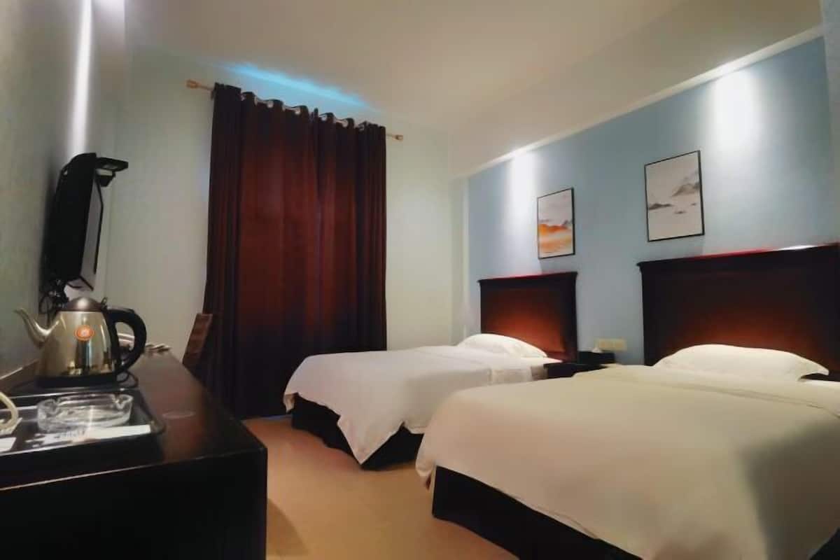 Une chambre d’hôtel avec deux lits, un bureau avec une bouilloire et un rideau.