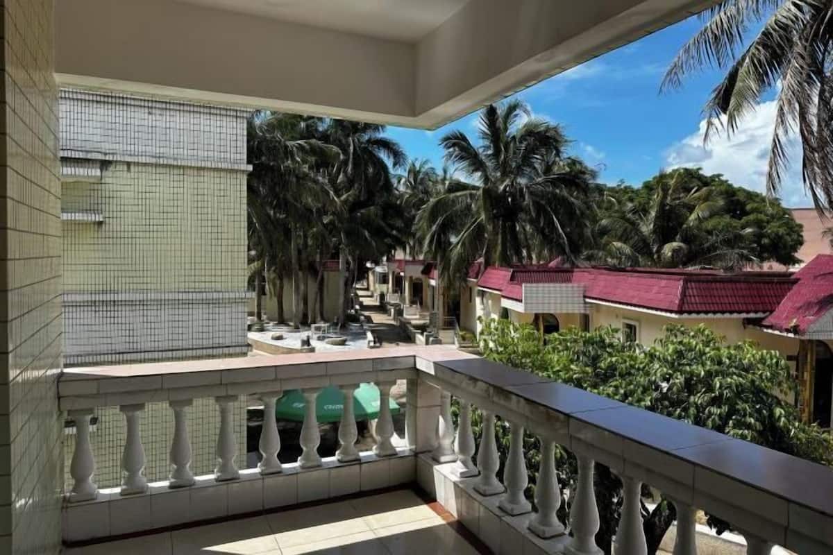 Un balcon doté d’un sol carrelé, d’une balustrade blanche et offrant une vue sur des palmiers et des immeubles.