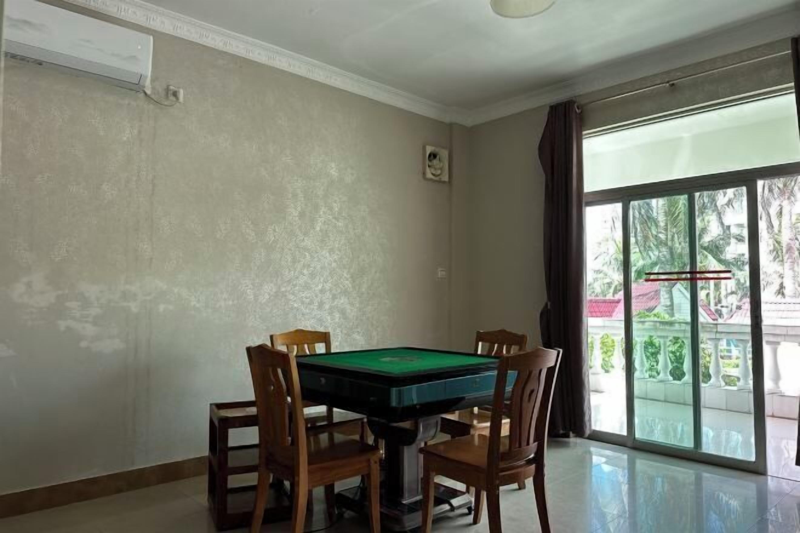 A room with a pool table, four wooden chairs, a ceiling fan, and a large window with a view of greenery.