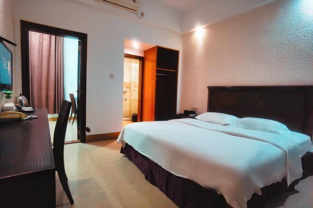 Une chambre d’hôtel avec un lit, un bureau et une chaise. Une porte donne accès à une salle de bain.