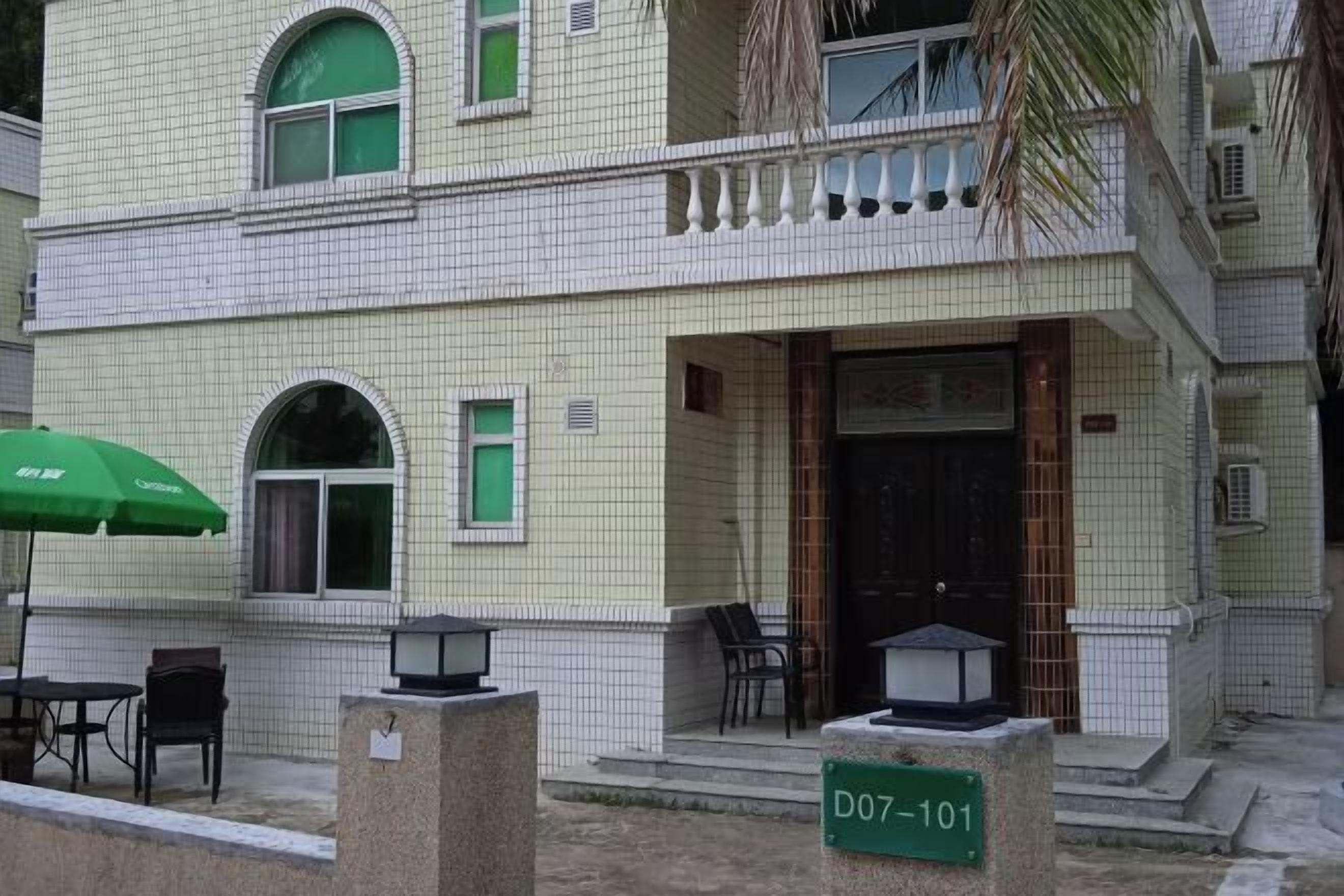 A building with a tiled facade, a balcony with a railing, and a door with a sign.