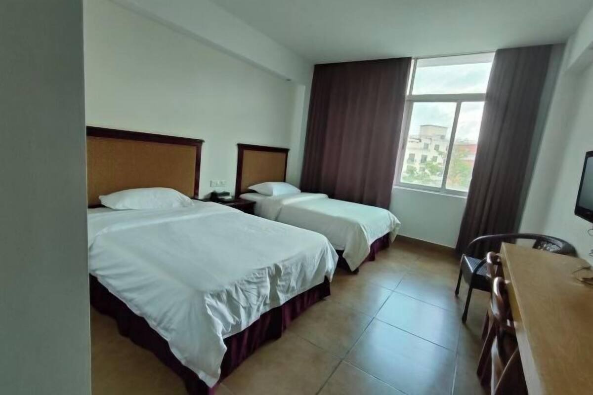 Une chambre d’hôtel avec deux lits, un bureau, une chaise et une fenêtre avec des rideaux.