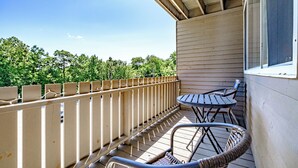 Un espacio al aire libre cubierto con una terraza de madera, sillas de metal y una mesa.