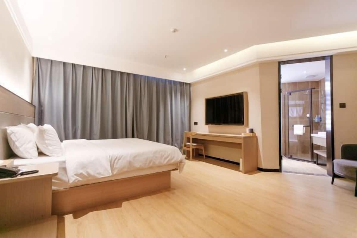 A modern hotel room with a large bed, a desk, and a glass shower area.