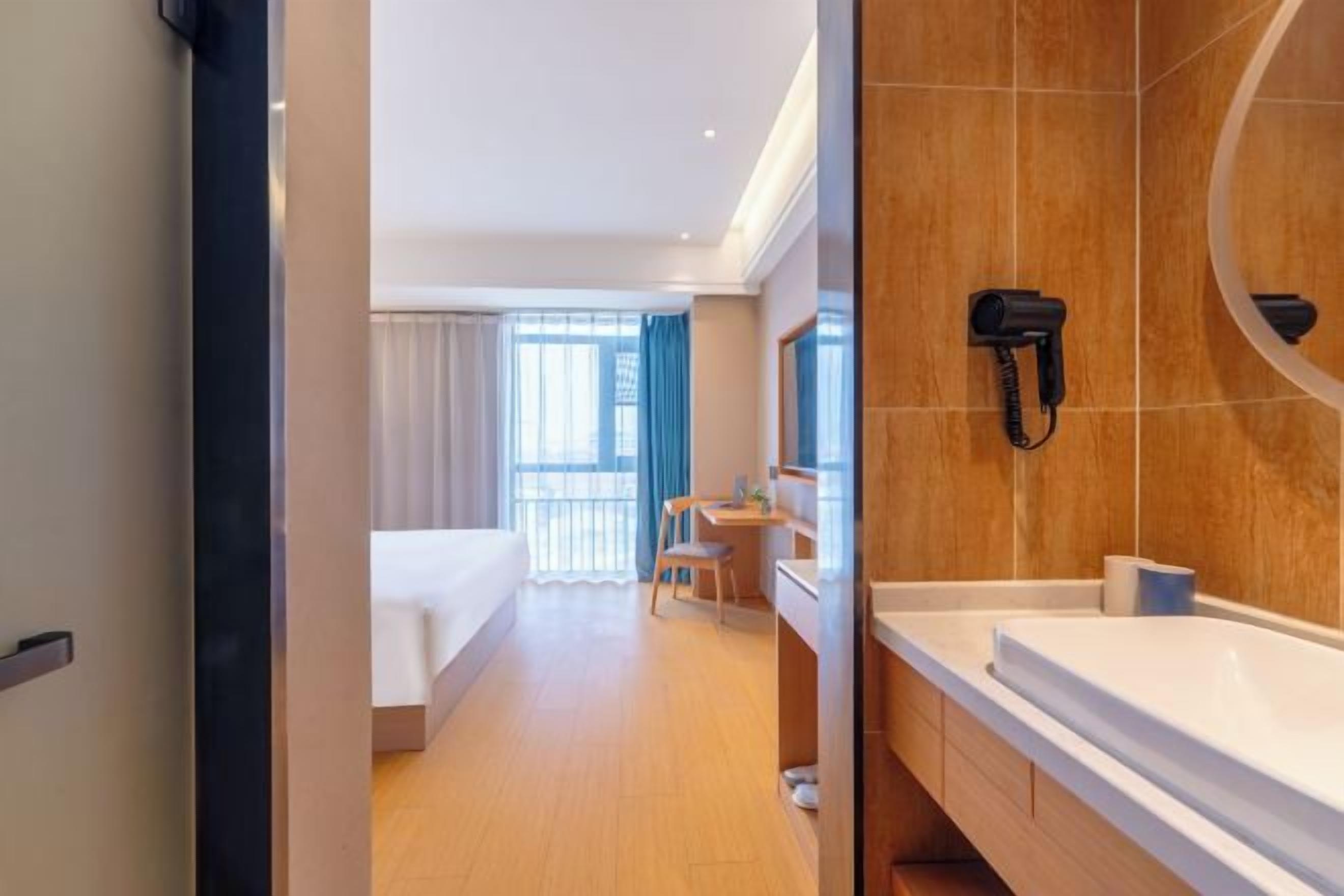 A hotel room with a bed, a desk, a chair, a bathroom with a sink and mirror, and a phone on the wall.