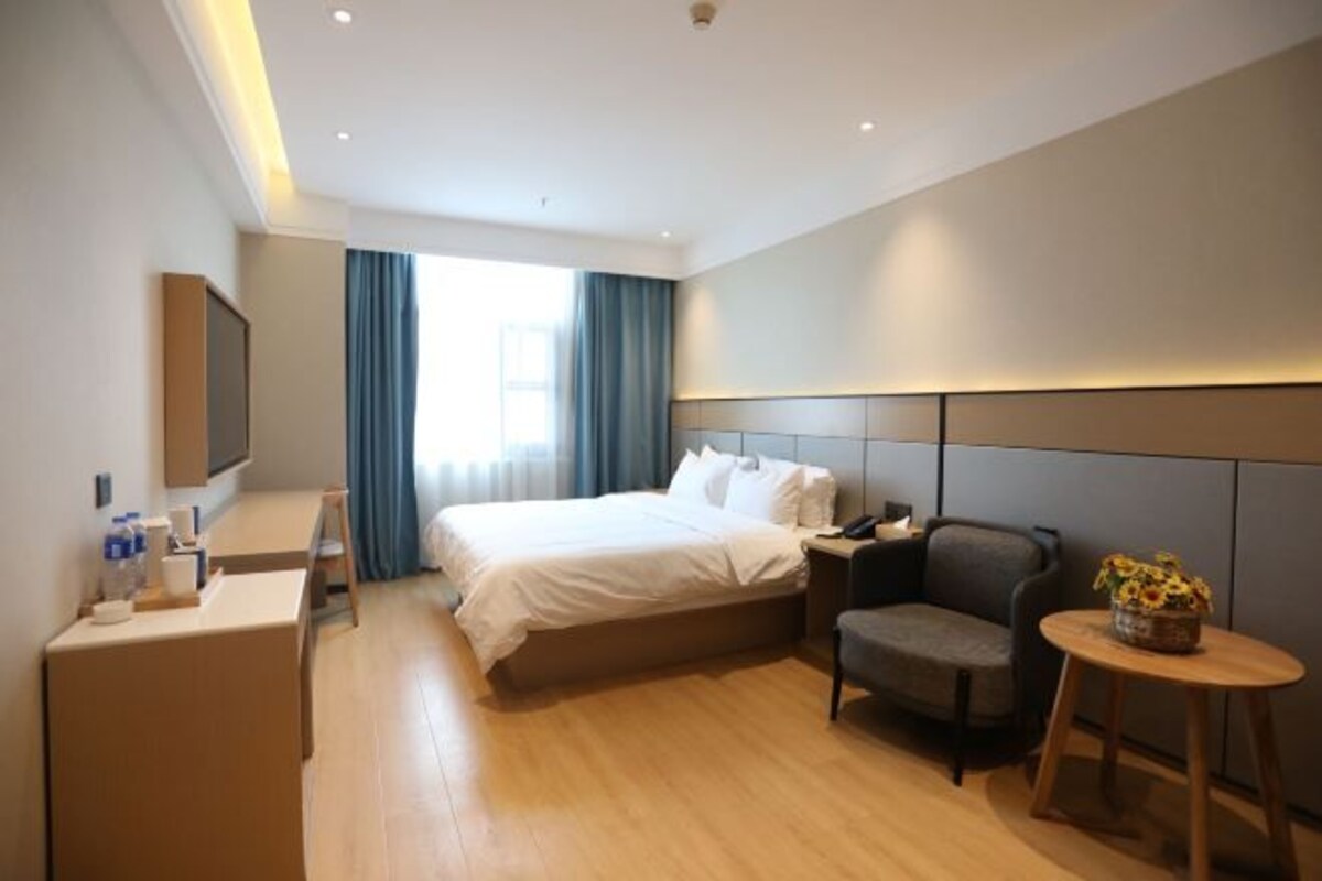 A hotel room with a bed, a desk, a chair, a small table, and a TV.