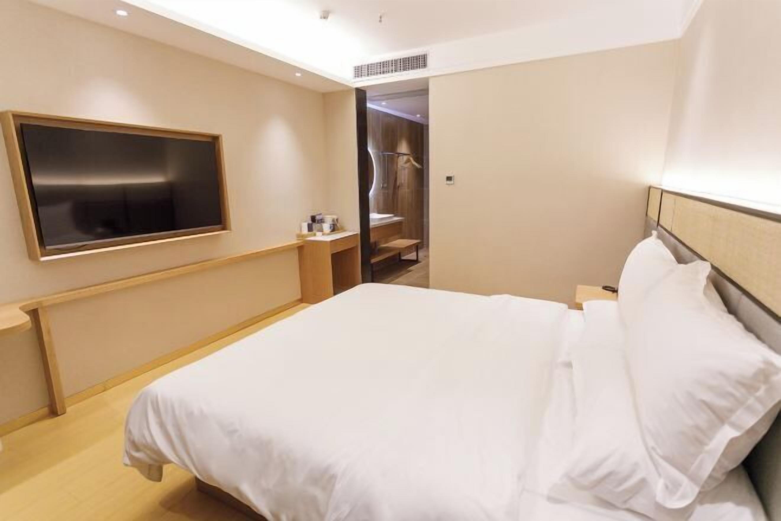 Een hotelkamer met een bed, een aan de muur bevestigde televisie, een houten nachtkastje en een inloopkast.