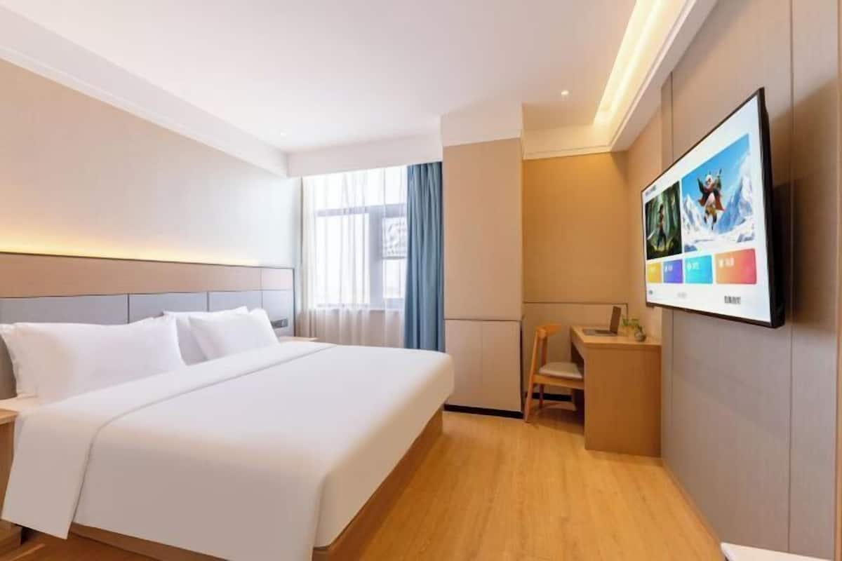 A hotel room with a bed, a desk, a chair, a TV, and a window with curtains.