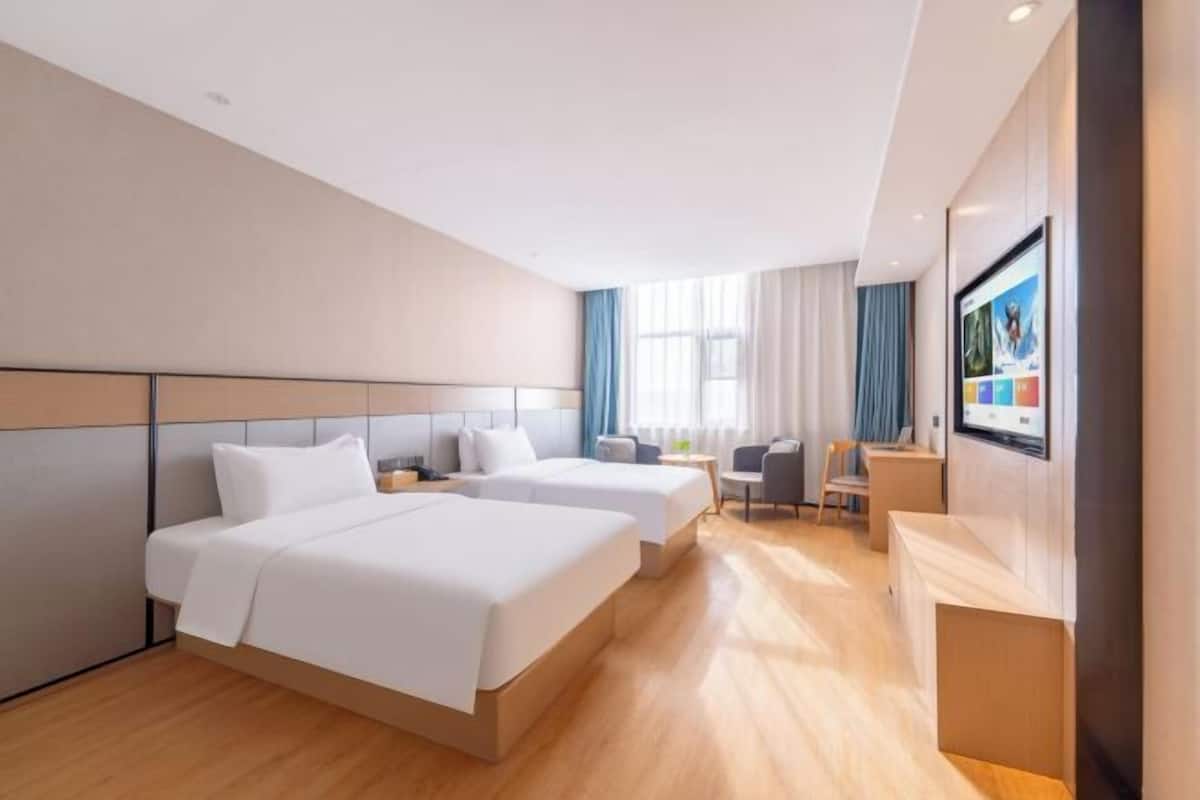 A hotel room with two beds, a desk, a chair, and a TV.