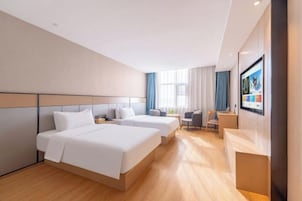 Habitación de hotel con dos camas, un escritorio, una silla y un televisor.