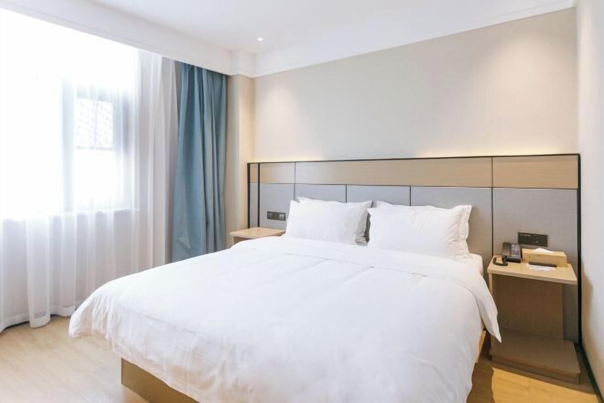 Une chambre d’hôtel moderne avec un grand lit, une table de chevet et une fenêtre avec des rideaux.