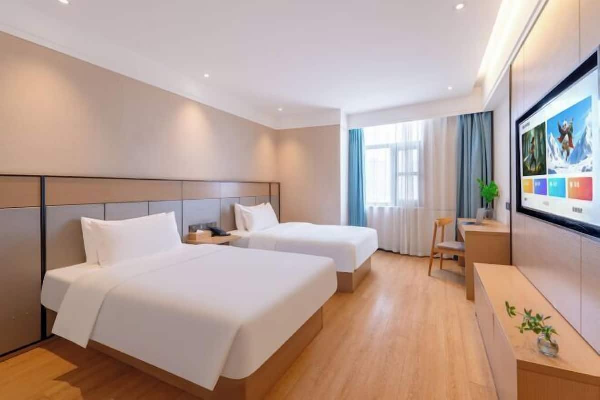 A hotel room with two beds, a desk, a chair, and a large TV screen.