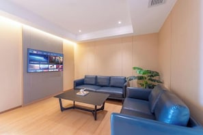 Ein modernes Wohnzimmer mit einem an der Wand befestigten Flachbildfernseher, einem blauen Ledersofa, einem dunklen Couchtisch und einem Topf mit Pflanze.