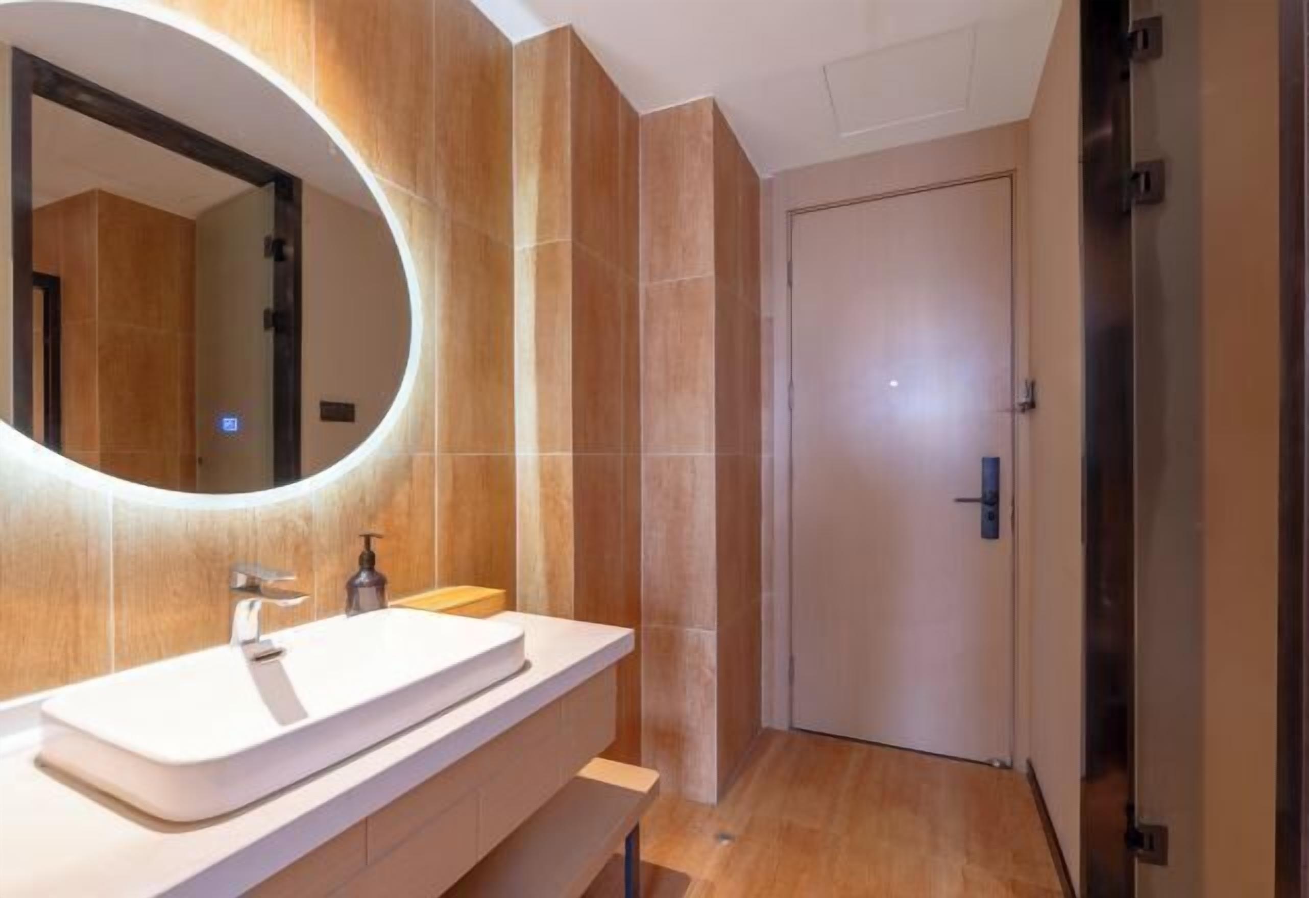 A modern bathroom with a large oval mirror, a white sink, and a wooden vanity.