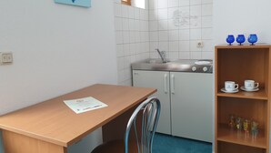 A small kitchenette with a sink, a wooden table, and a chair. There is a shelf with cups and jars. - Siegmundsburger Haus Werraquelle here apartment "Rennweg" - ground floor, pet friendly (Siegmundsburg)