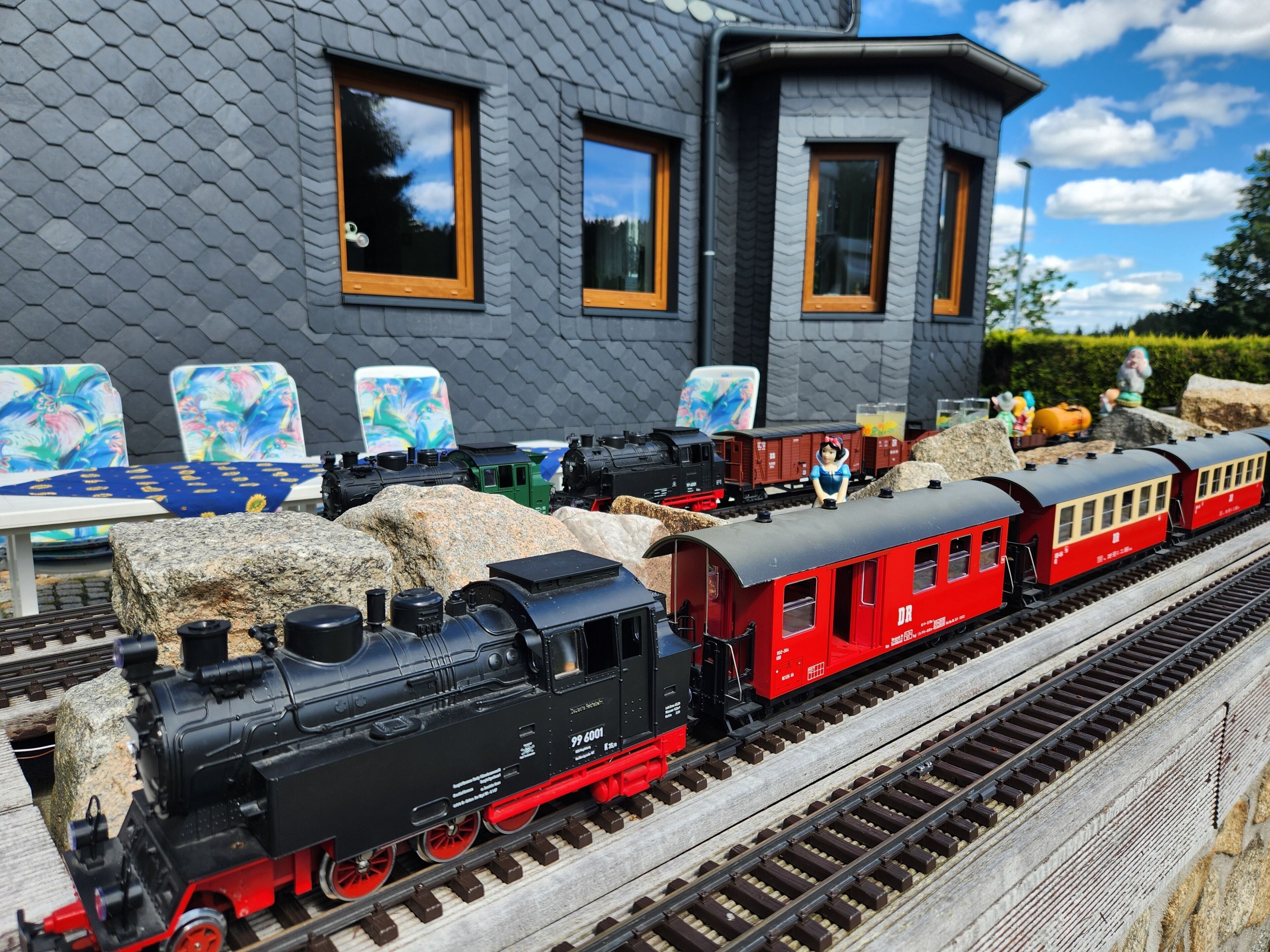 Un modellino di treno con una locomotiva nera, vagoni passeggeri rossi e una piccola statuetta.