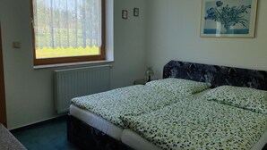 A bedroom with a bed, a window with curtains, a radiator, a lamp, and a framed picture on the wall. - Siegmundsburger Haus Werraquelle here apartment "Rennweg" - ground floor, pet friendly (Siegmundsburg)