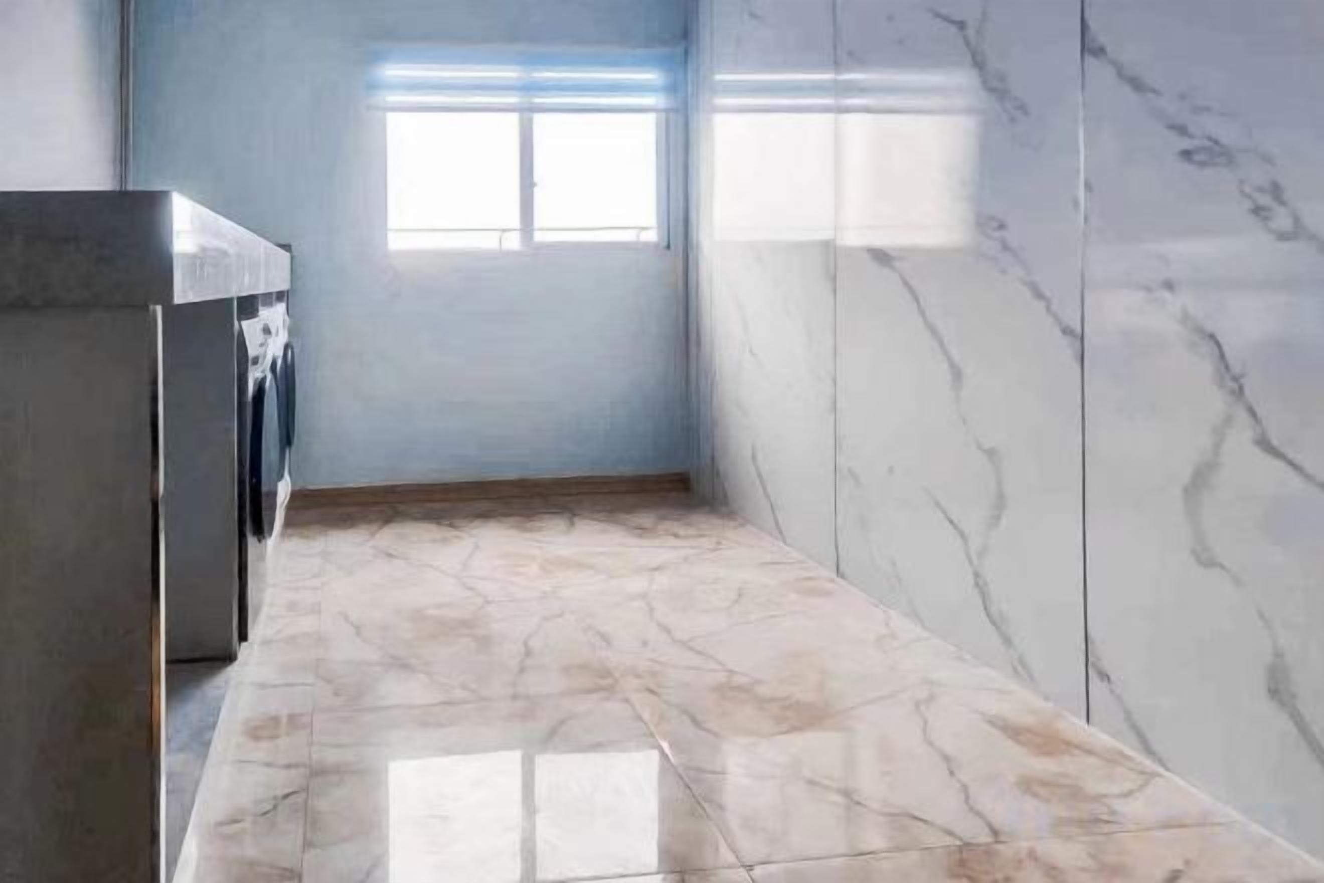 A narrow hallway with a washing machine, a window, and marble walls.