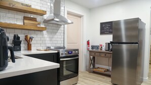 A modern kitchen with a stainless steel refrigerator, an oven, a coffee maker, and a chalkboard with a message.