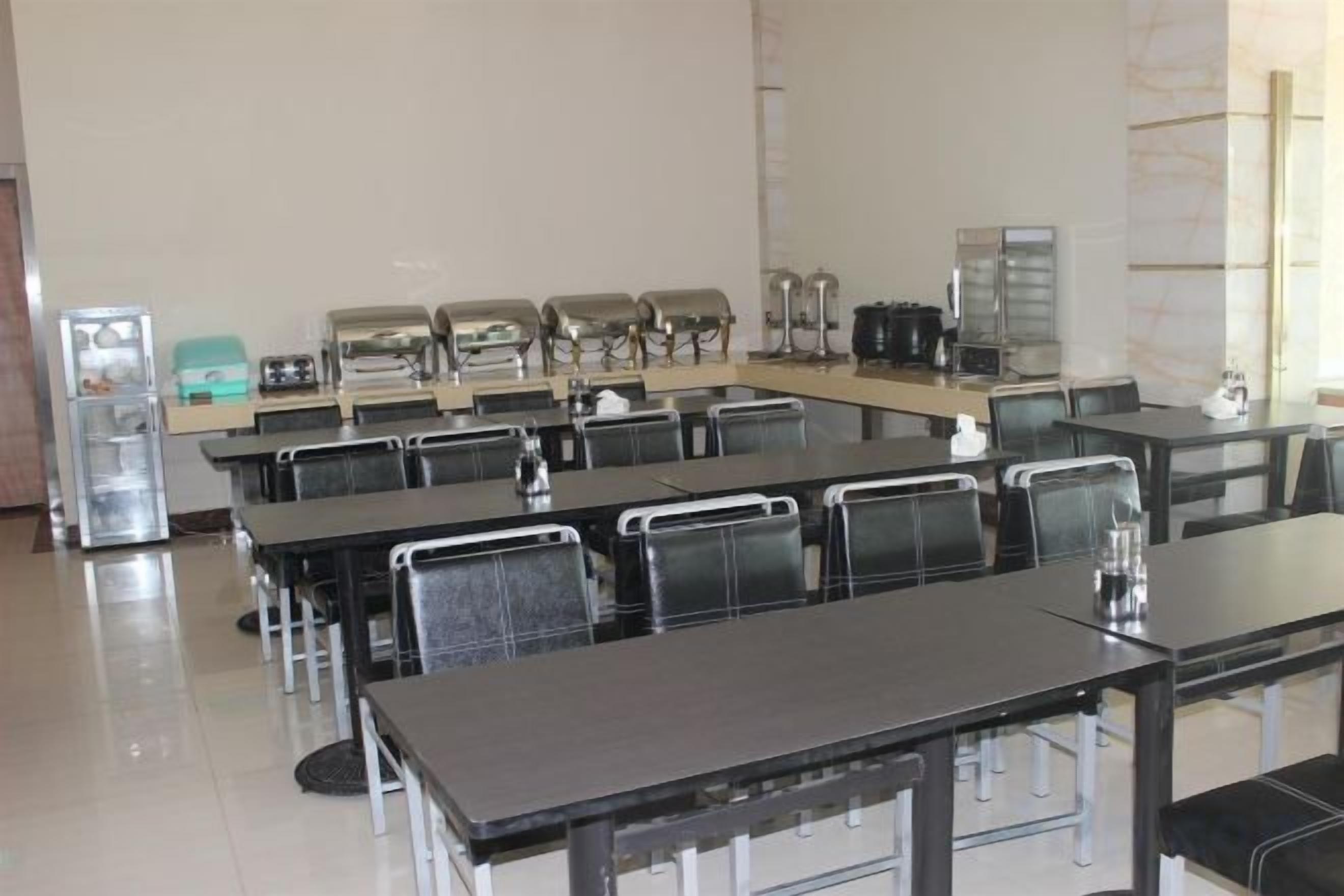 A conference room with multiple tables and chairs, equipped with coffee makers and a refrigerator.