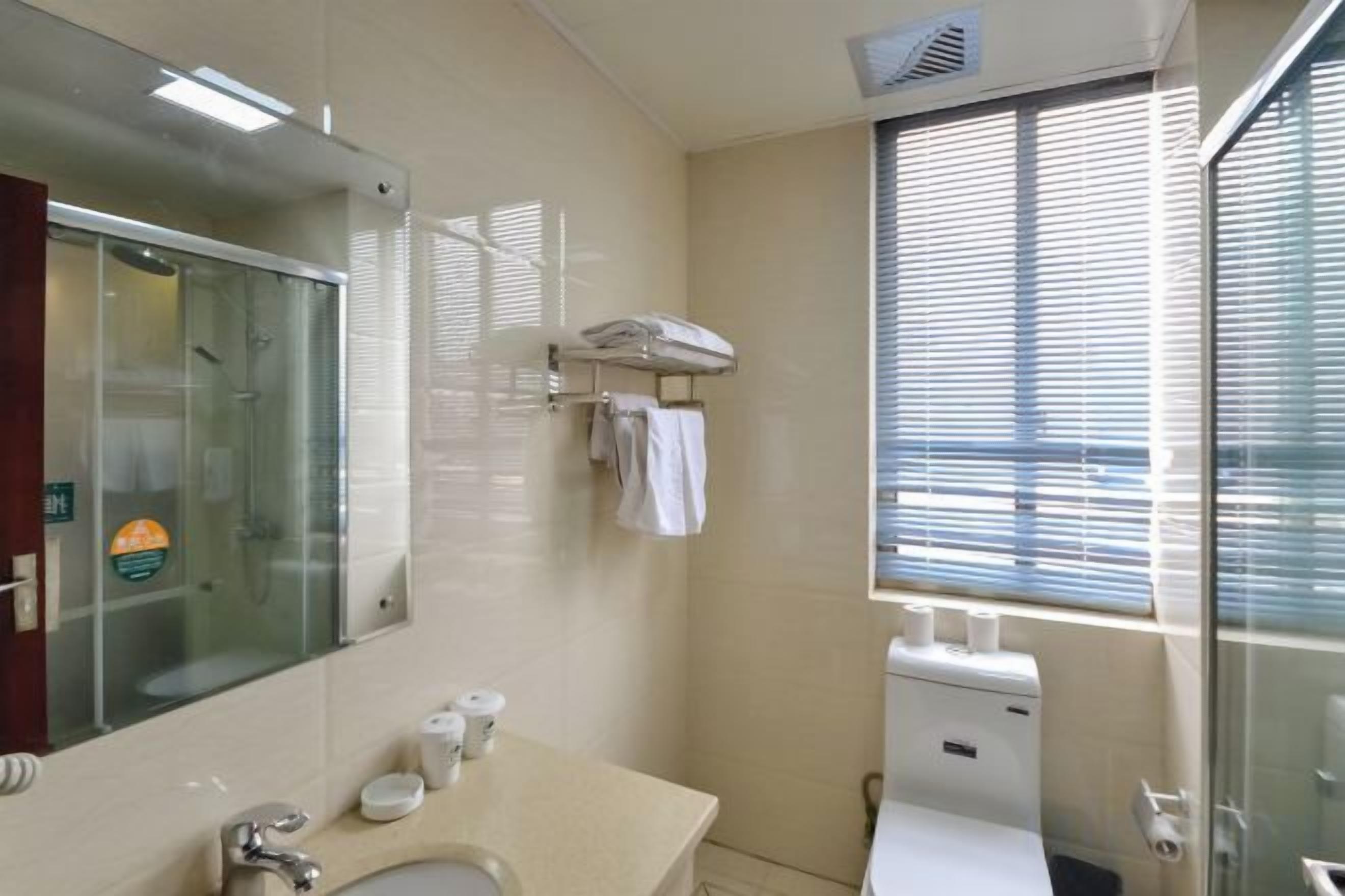 Ein Badezimmer mit Waschbecken, Spiegel, Handtuchhalter und einem Fenster mit Jalousien.