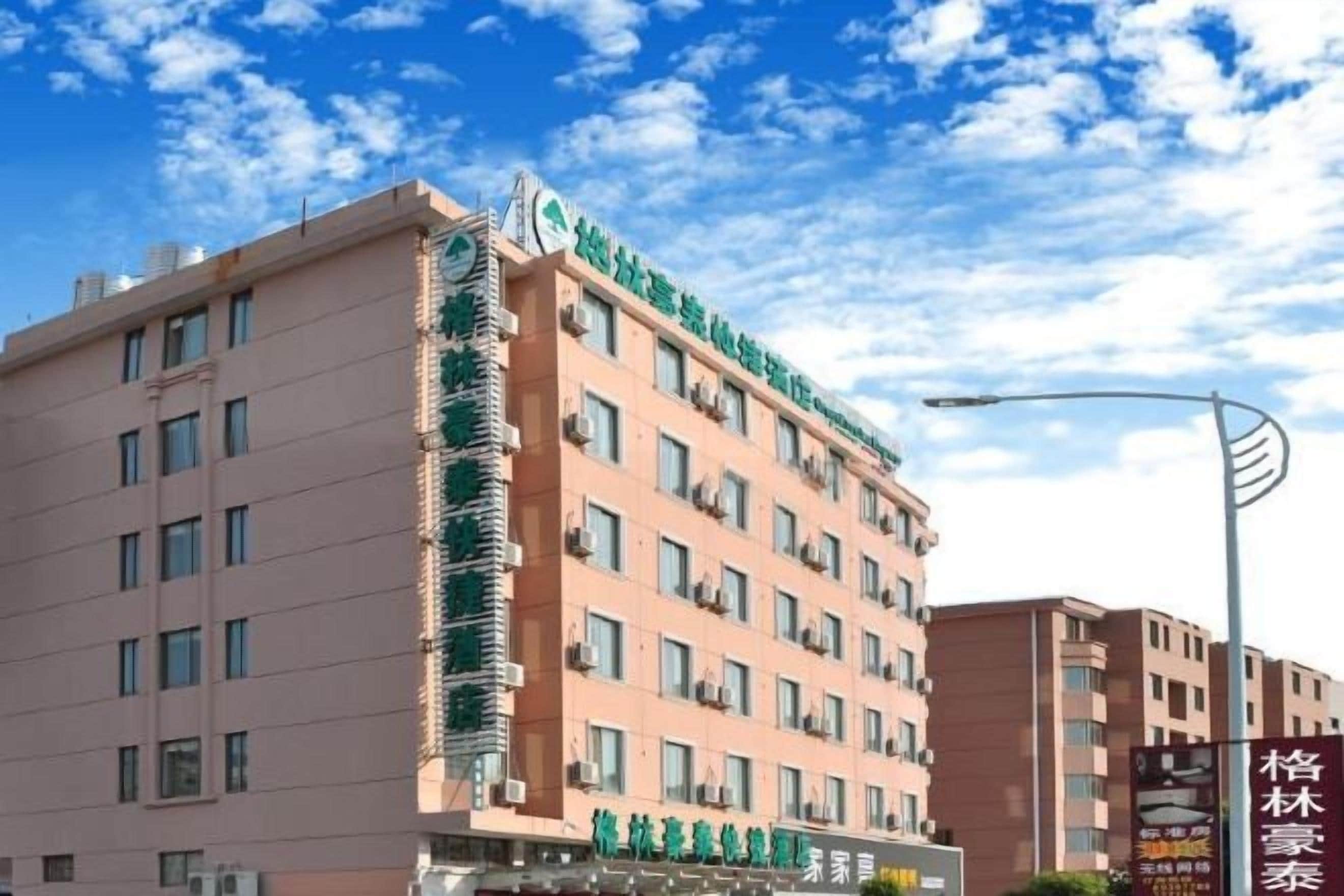 A multi-story hotel with a prominent green sign on the facade, multiple windows, and a clear sky in the background.