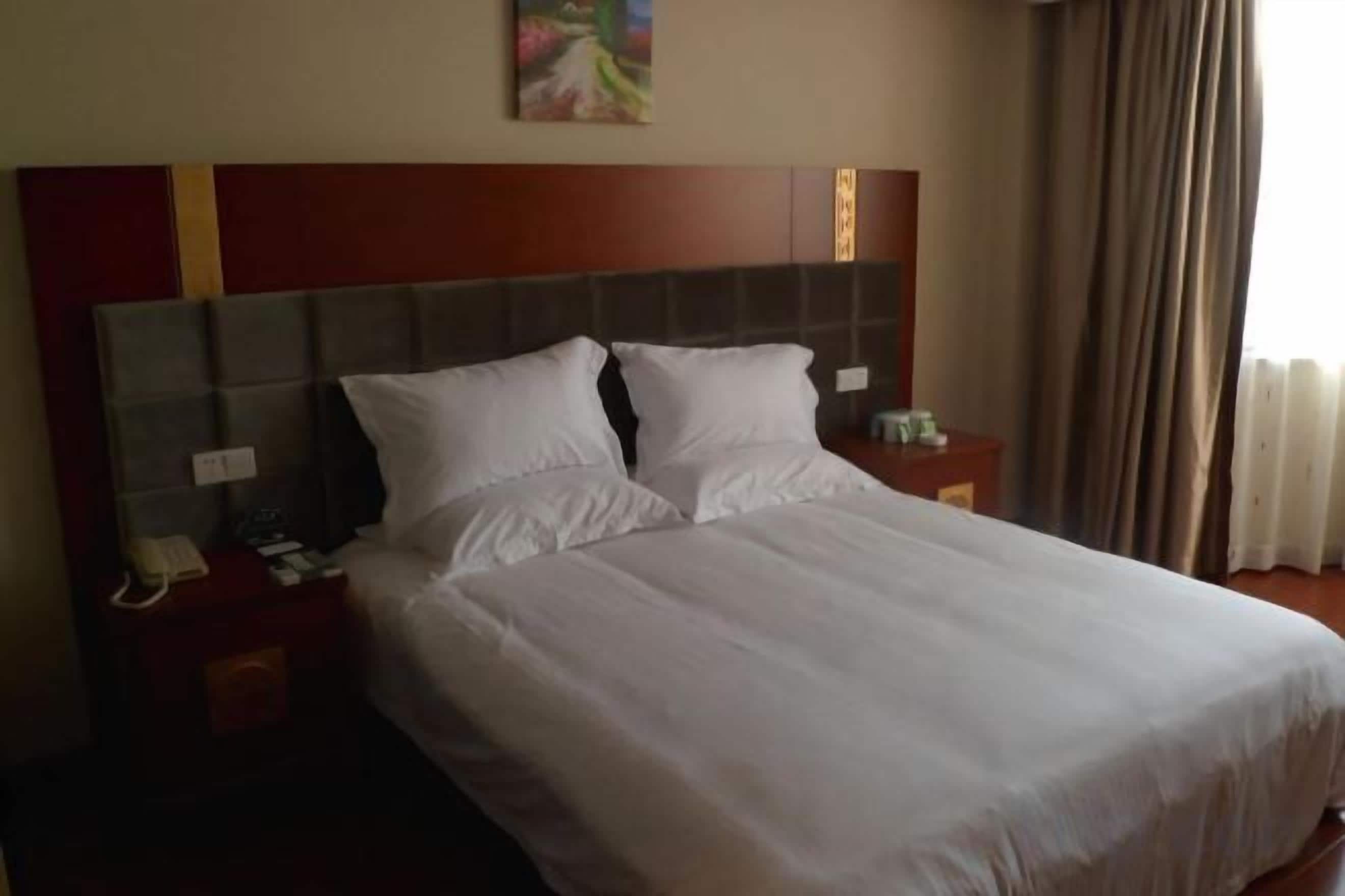 Een hotelkamer met een groot bed, een houten hoofdeinde, een nachtkastje met een telefoon en een raam met gordijnen.