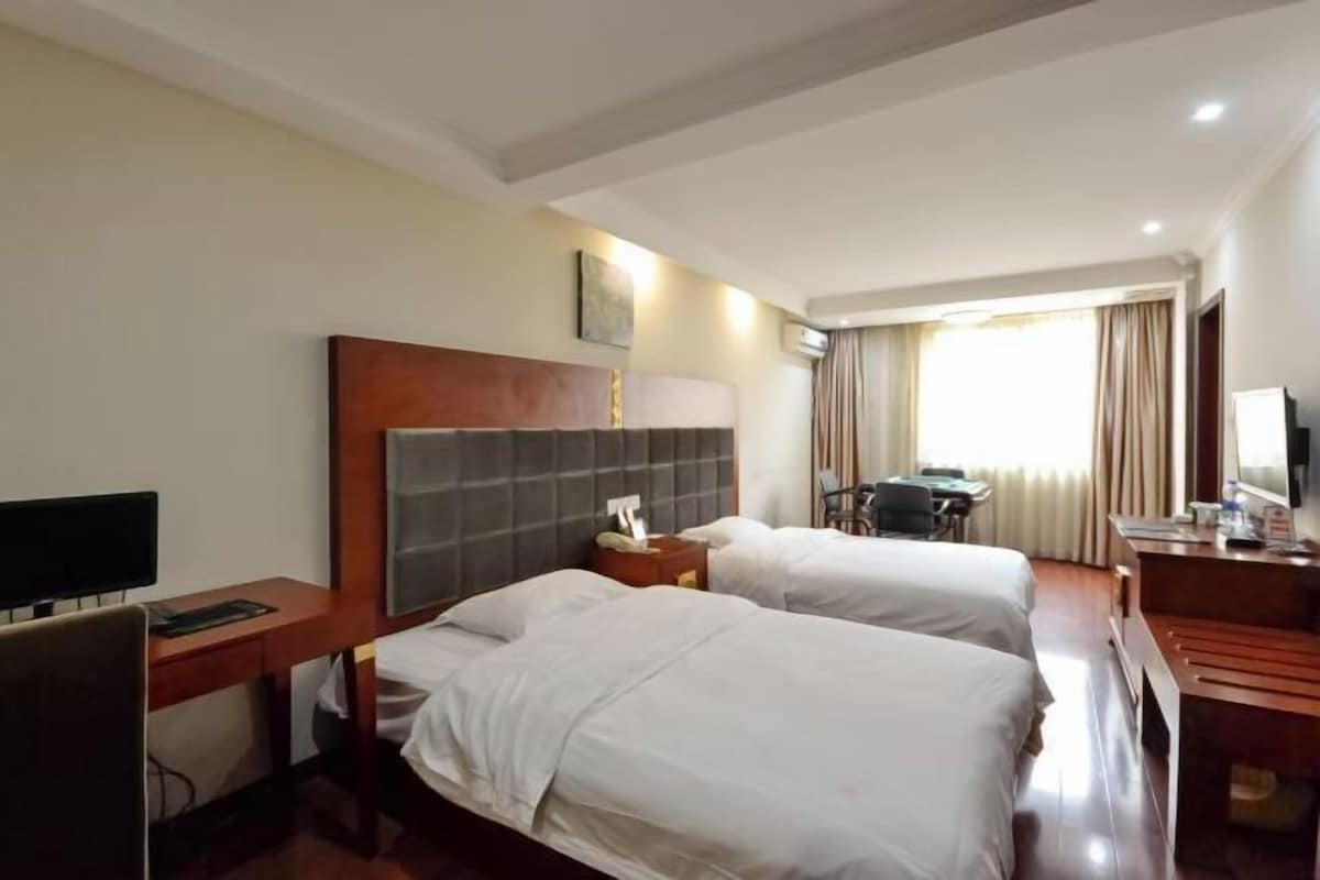 A hotel room with two beds, a desk, a chair, a television, and a window with curtains.