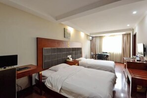 A hotel room with two beds, a desk, a chair, a television, and a window with curtains.