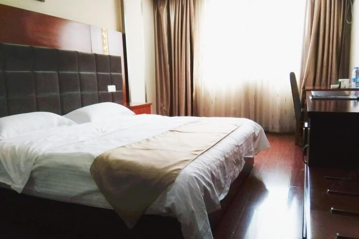 A hotel room with a bed, a wooden headboard, a desk with a chair, and curtains.