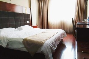 A hotel room with a bed, a wooden headboard, a desk with a chair, and curtains.