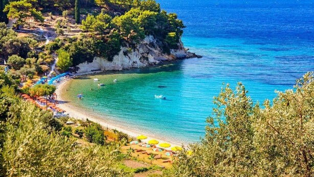 Une plage côtière aux eaux d’un bleu limpide, avec un rivage sablonneux et quelques parasols.