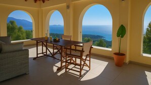 Un espace repas comprenant une table et des chaises, de grandes fenêtres en arc de cercle et une plante en pot.