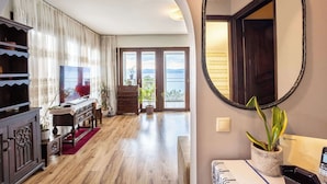 A spacious room with a wooden floor, a large mirror, a potted plant, and a view of the outdoors through a glass door. - Endless Blue Seafront Retreat - Mikra Mantineia (Paralia Vergas)