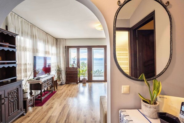 A spacious room with a wooden floor, a large mirror, a potted plant, and a view of the outdoors through a glass door.